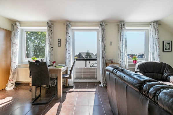 A living room with a sofa, a dining table with chairs, and a view through a glass door to an outdoor area.