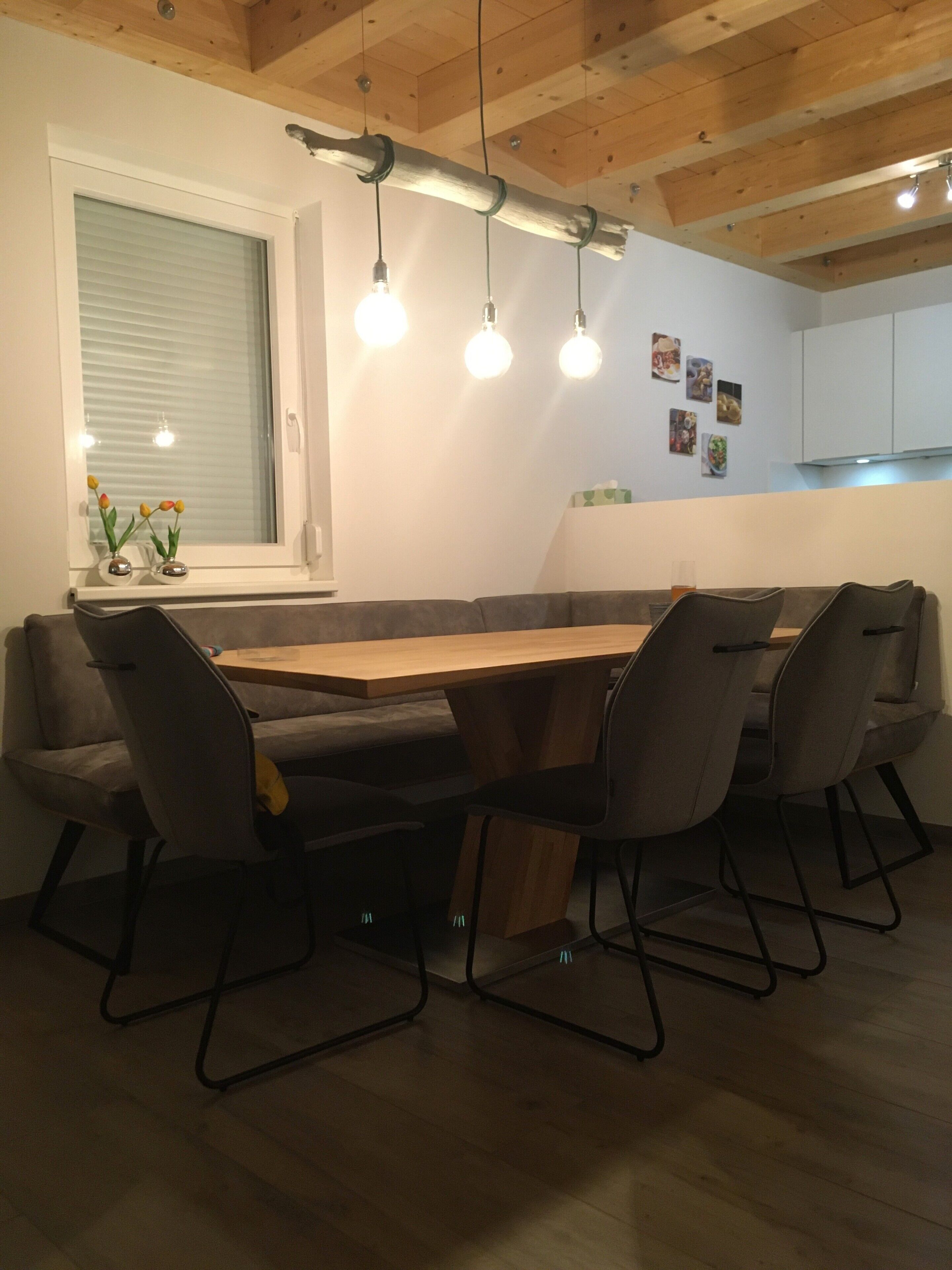 A dining area with a wooden table, four chairs, a window with blinds, and pendant lights.