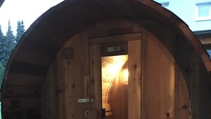 Una struttura a forma di botte in legno, con una porta, una panchina e un tavolino.