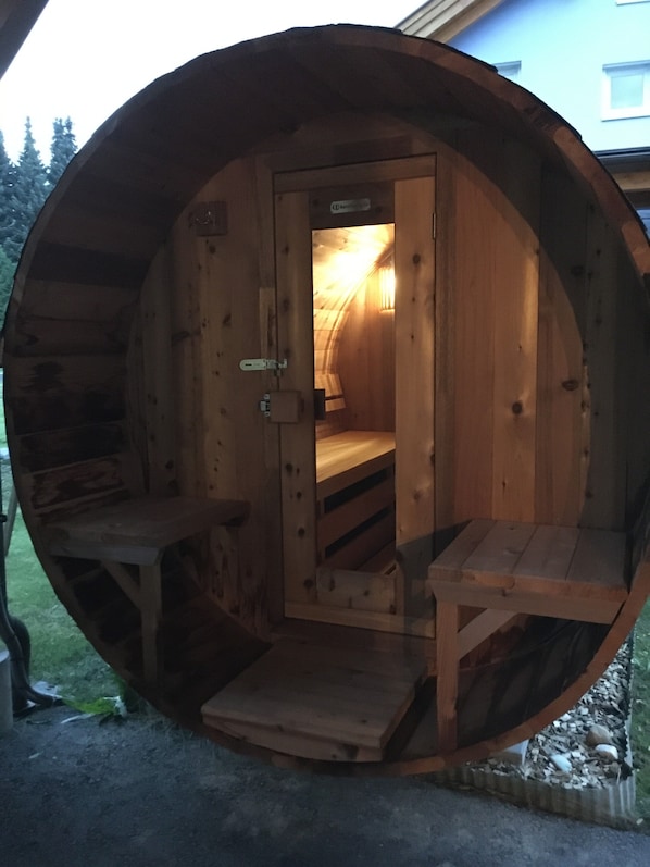 A wooden barrel-shaped structure with a door, a bench, and a small table.