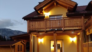 Una casa a due piani in legno con un balcone, un patio coperto e una zona pranzo con sedie.