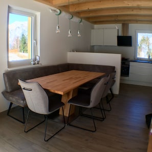A modern kitchen with a wooden dining table, grey chairs, and a built-in island.