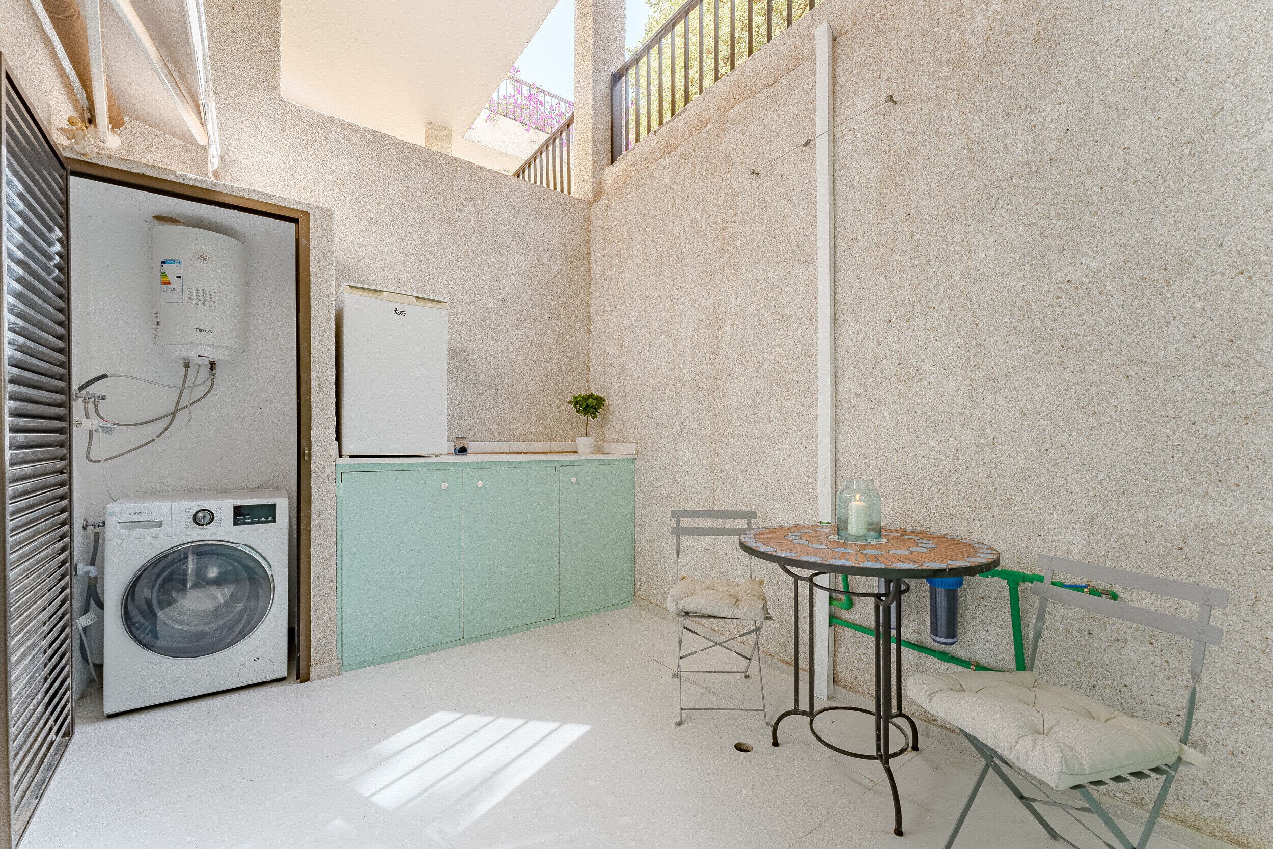 A compact kitchen with a washing machine, a refrigerator, and a small dining table with a chair.