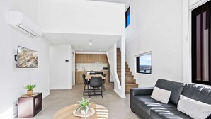 A modern living room with a grey sofa, a round wooden coffee table, and a dining area with a wooden table and chairs.