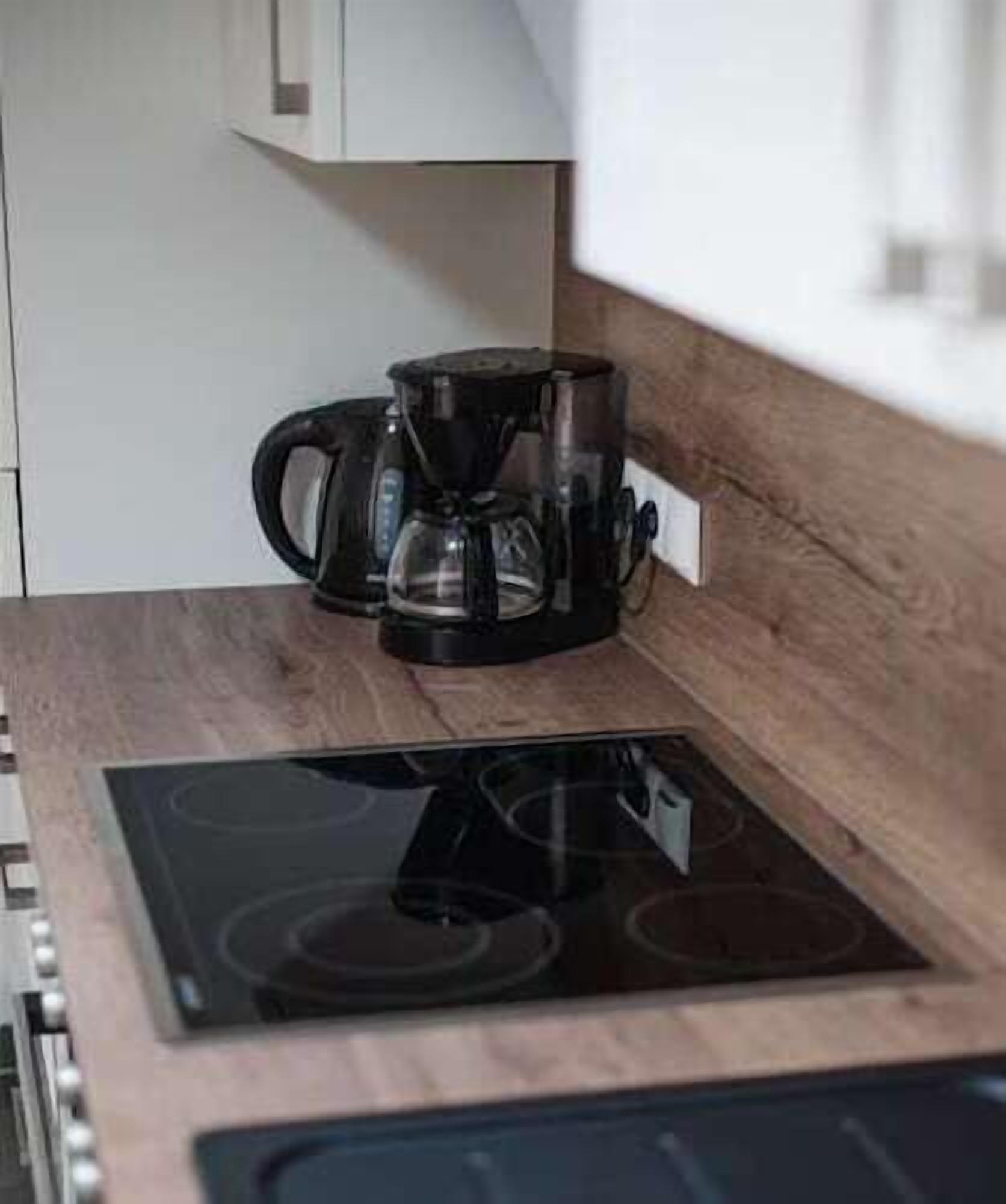 A kitchen with a black coffee maker on a wooden countertop and a black induction cooktop.
