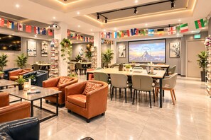 Un moderno vestíbulo de hotel con asientos de cuero, una amplia mesa de comedor y una pantalla de televisión que muestra una vista panorámica.