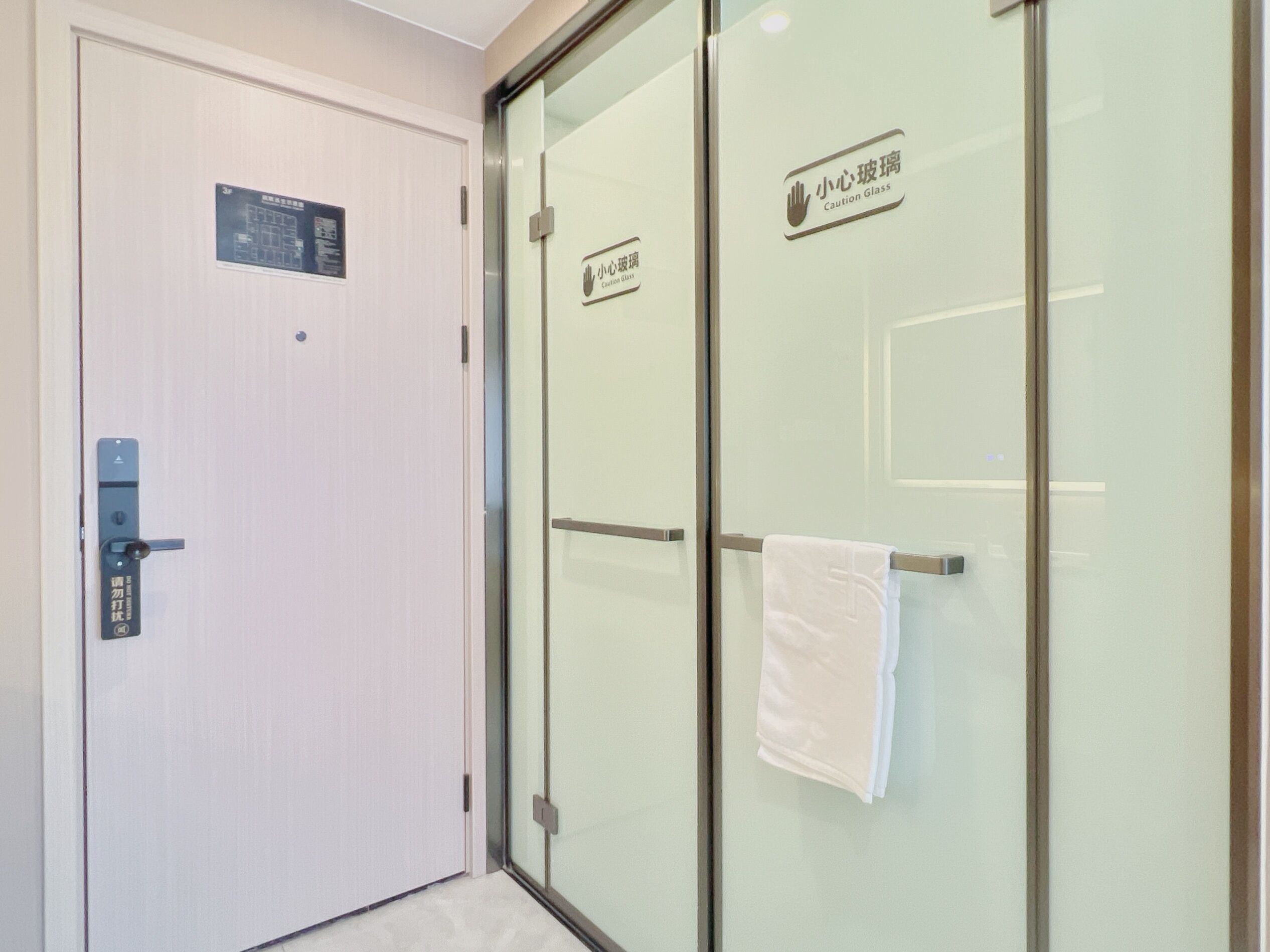 A hotel room with a white door, a glass partition, and a towel hanging on the partition.