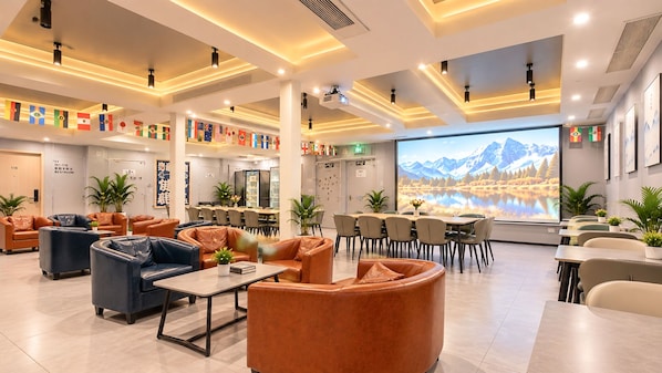 A modern hotel lobby with leather sofas, a dining area, and a large screen displaying a mountain landscape.