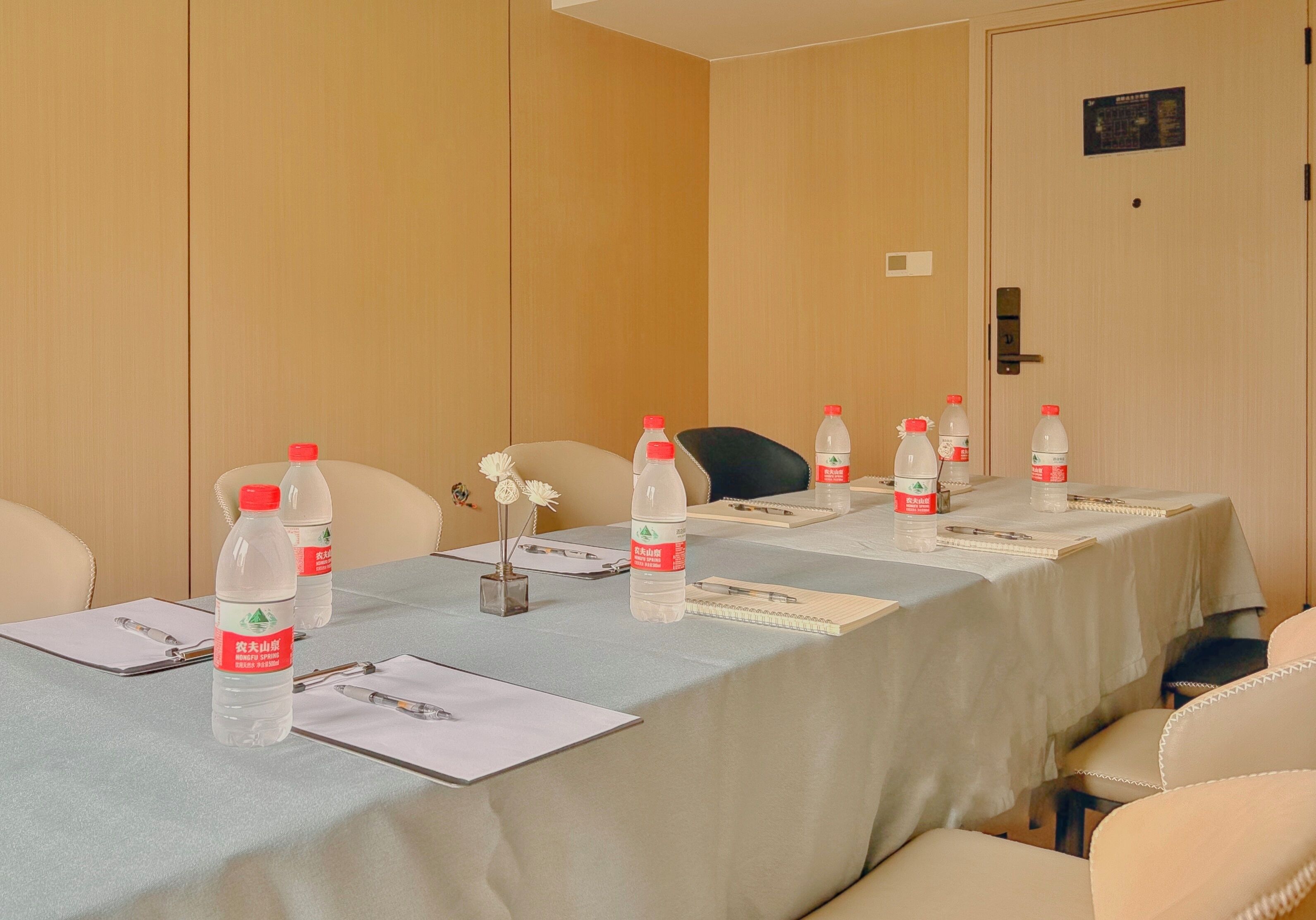A conference room with a long table, chairs, water bottles, notepads, pens, and a small vase with flowers.