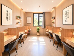 Un salón de estudio con escritorios de madera, sillas negras y plantas en macetas.