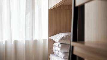 A neatly made bed with white linens, a wooden headboard, and a window with sheer curtains.