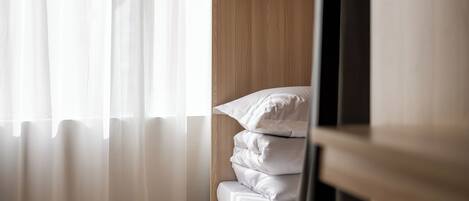 A neatly made bed with white linens, a wooden headboard, and a window with sheer curtains.