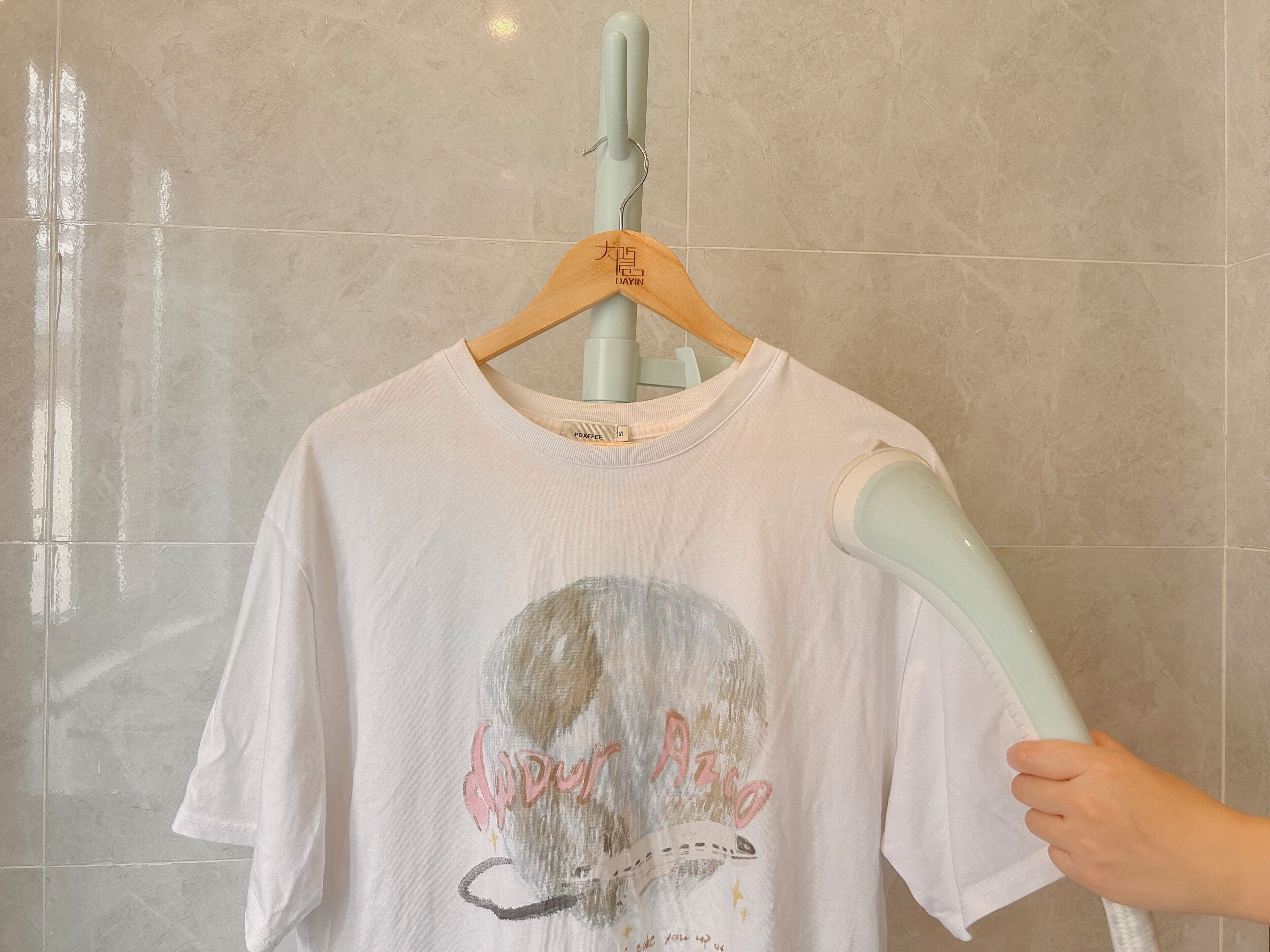 A white t-shirt with a skull graphic and text hanging on a wooden hanger.