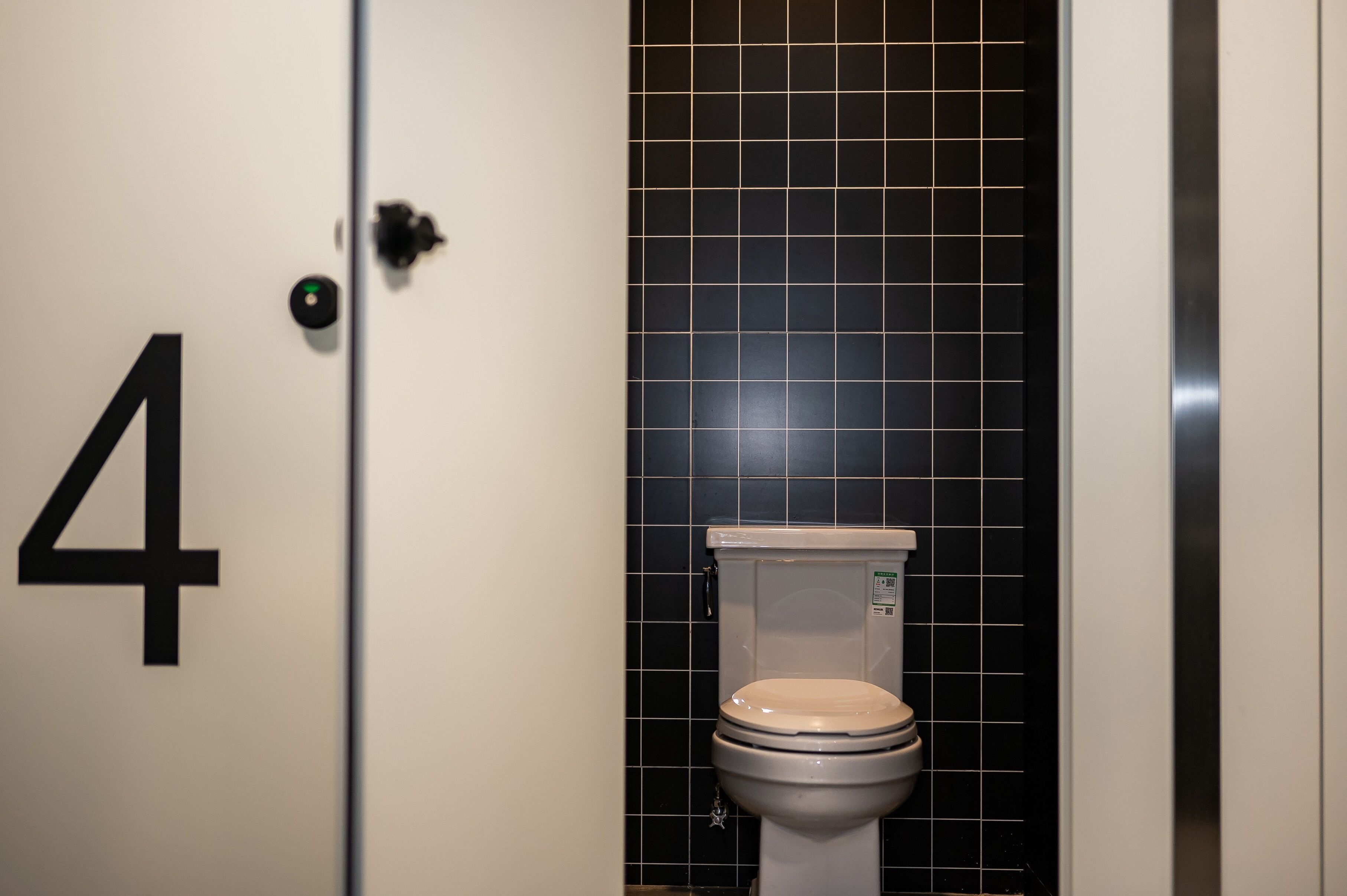A bathroom with a toilet, black tiled walls, and a door marked with the number 4.
