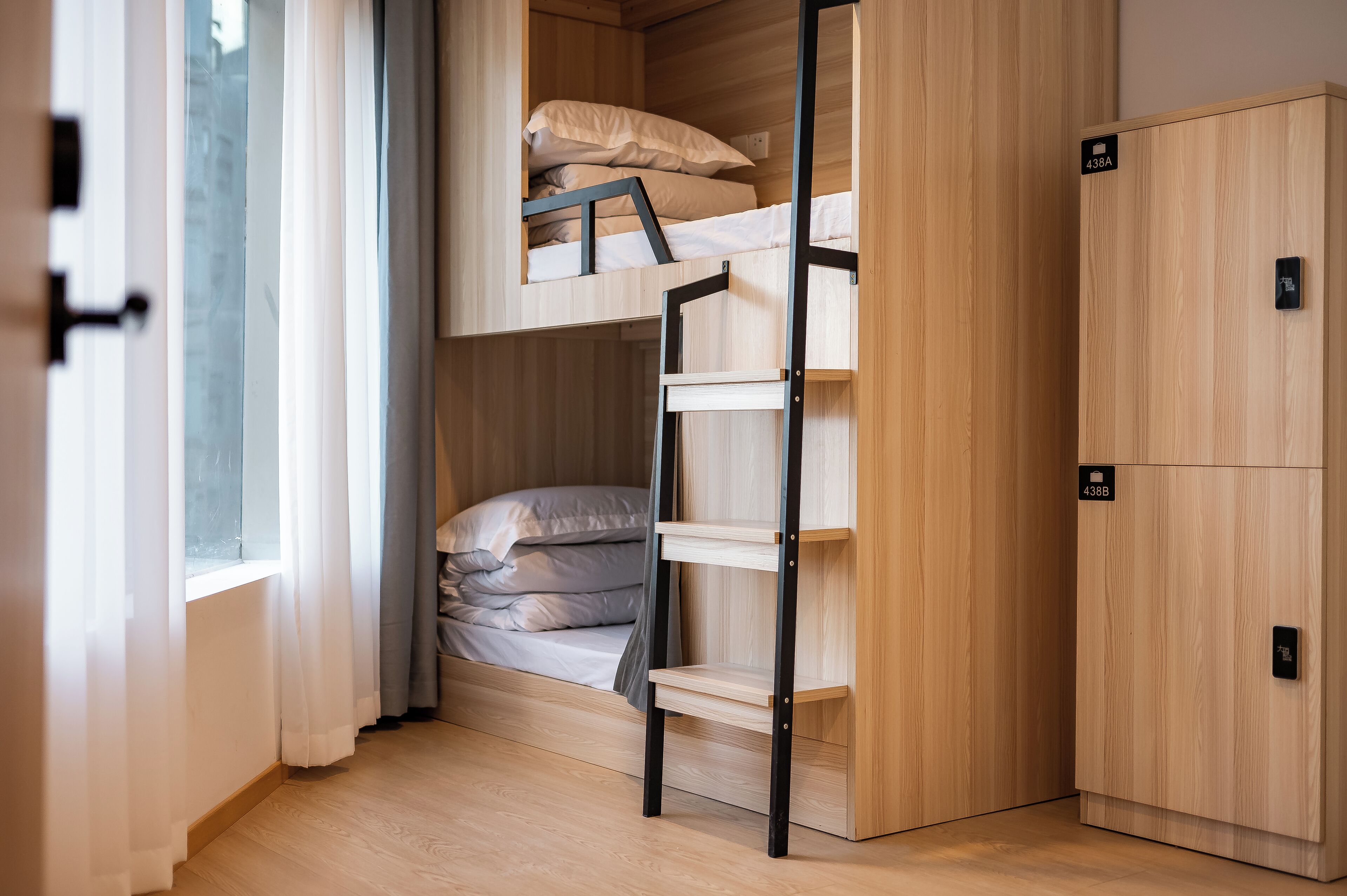 A compact room with a bunk bed, a wooden wardrobe, and a window with curtains.
