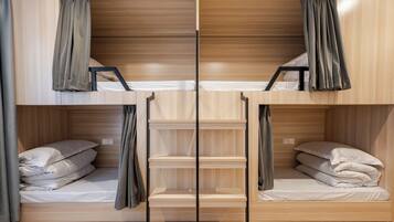 Dormitorio con literas, paredes de madera y cortinas. Hay dos camas, cada una con una almohada y una colcha.