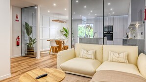 A modern living room with a beige sofa, a wooden coffee table, and a glass partition separating the living area from the kitchen. - Machico Fachos View, a Home in Madeira (Machico)