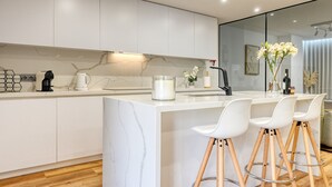 A modern kitchen with white cabinetry, a marble backsplash, and a central island with bar stools. - Machico Fachos View, a Home in Madeira (Machico)