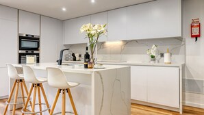 A modern kitchen with white cabinetry, a marble island, and bar stools. - Machico Fachos View, a Home in Madeira (Machico)
