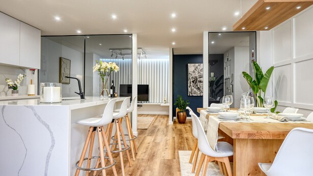 A modern kitchen with white bar stools, a wooden dining table set for four, and a large mirror reflecting the room. - Machico Fachos View, a Home in Madeira (Machico)