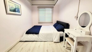 A bedroom with a bed, a bedside table, a mirror, and a window with blinds. - Nampo Hill guesthouse (Busan)