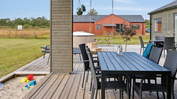 An outdoor patio with a wooden deck, a table and chairs, and a view of a red building in the background. - "Henke" - 475m from the sea by Interhome (Ålbæk)