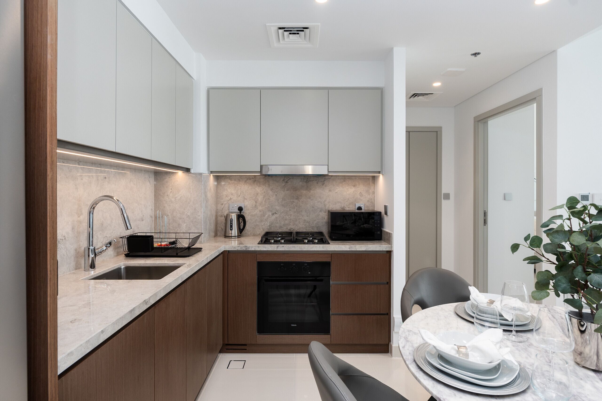 A modern kitchen with wooden cabinets, a built-in oven, and a dining area with a table set for two.