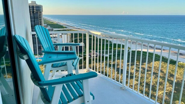 Un balcon avec deux fauteuils Adirondack turquoise donnant sur une plage et l’océan.