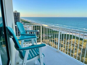 A balcony with two turquoise Adirondack chairs overlooking a beach and ocean.