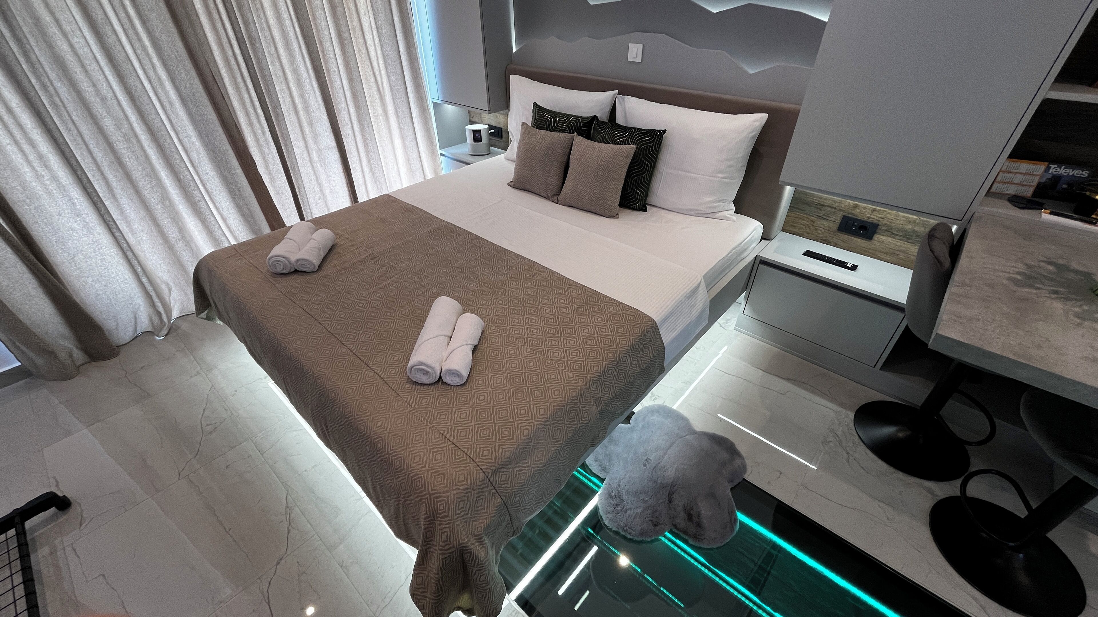 A modern hotel room with a large bed, a nightstand, a desk, and a chair.