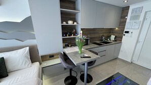 Una cocina moderna con estufa integrada, microondas y pileta. Hay un comedor con mesa y sillas, y un sofá en la zona de estar contigua.