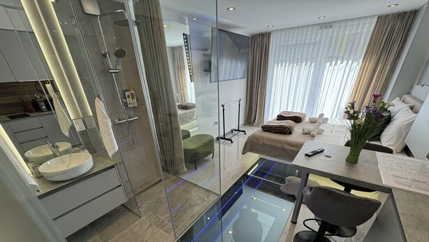 Un baño moderno con ducha envuelta en vidrio, tocador con un lavamanos grande y una zona de estar con mesa y sillas.