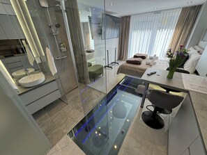 Un baño moderno con ducha envuelta en vidrio, tocador con un lavamanos grande y una zona de estar con mesa y sillas.