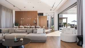 Ein modernes Wohnzimmer mit einer Eckcouch, einem runden Couchtisch und einem runden Akzentstuhl. Eine Holzpaneelwand beherbergt ein Regalsystem, und ein großes Fenster bietet einen Blick ins Freie.