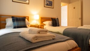 Une chambre d’hôtel avec deux lits, chacun étant équipé d’un oreiller et d’une couverture. Une table de chevet avec une lampe se trouve entre les deux lits.