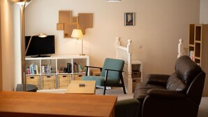 Un salon comprenant un téléviseur, un canapé, un fauteuil, une lampe et une bibliothèque.