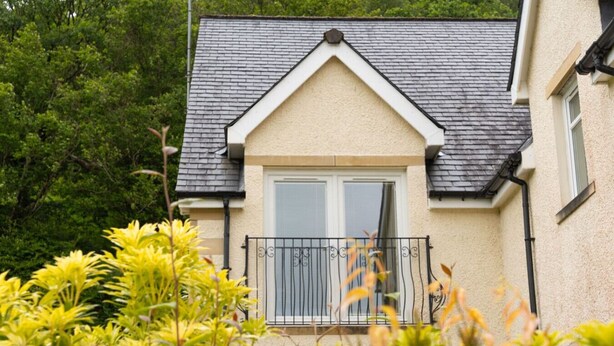 Une maison avec un toit à pignon, une porte d’entrée et un petit balcon doté d’une rambarde en métal.
