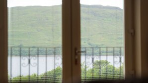 Une vue à travers une fenêtre ornée d’une rambarde en métal, donnant sur une étendue d’eau et des collines verdoyantes.