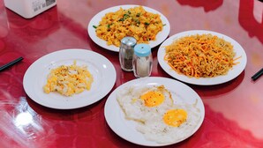Una mesa con cuatro platos de comida, entre ellos huevos fritos y fideos.