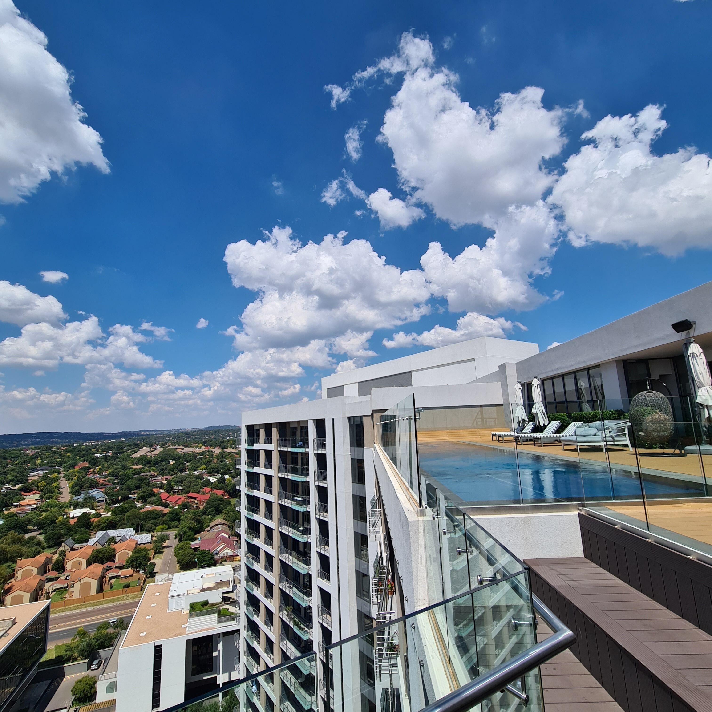 A modern building with a glass facade, a rooftop pool, and a view of a residential area.
