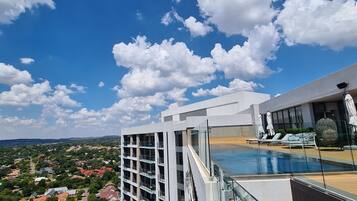 A modern building with a glass facade, a rooftop pool, and a view of a residential area.
