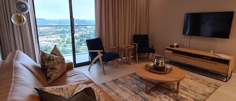 A modern living room with a large window, a sofa, two armchairs, a coffee table, and a flat-screen TV.