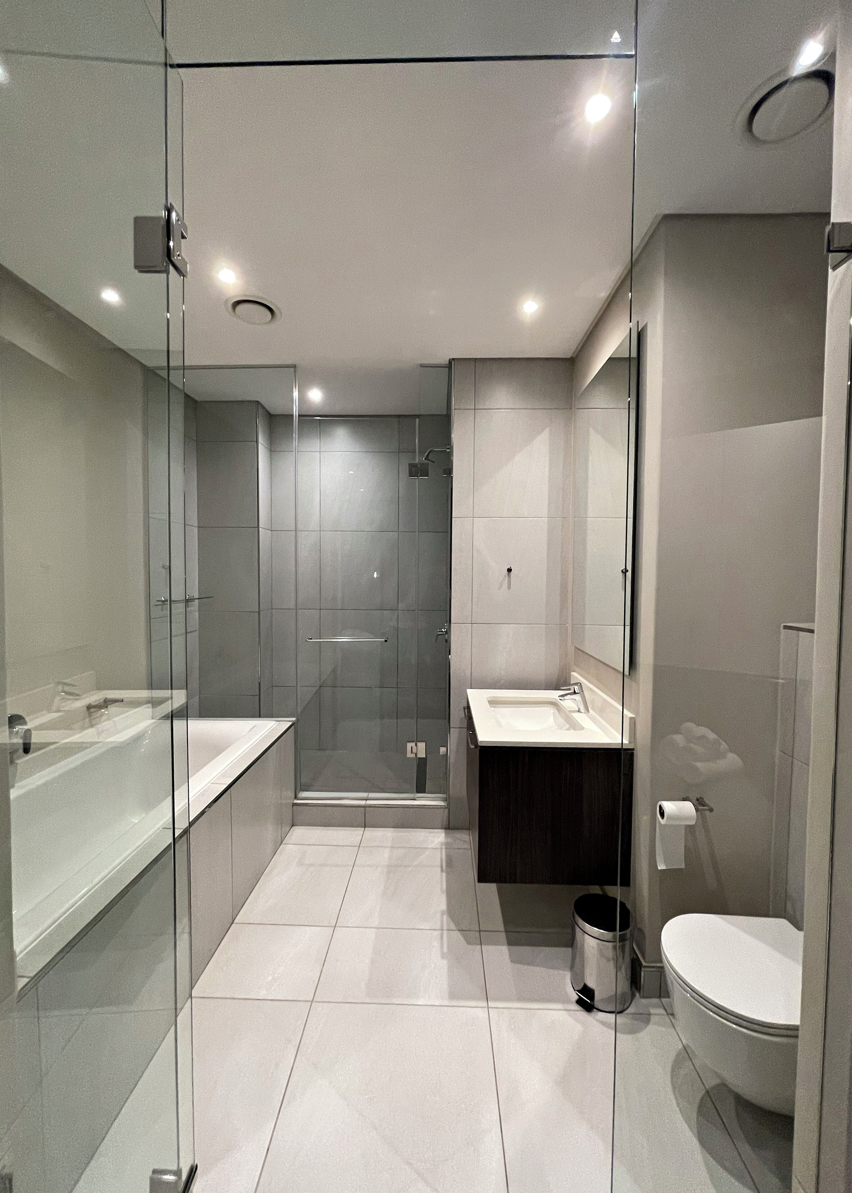 A modern bathroom with a glass-enclosed shower, a white bathtub, and a separate sink area.