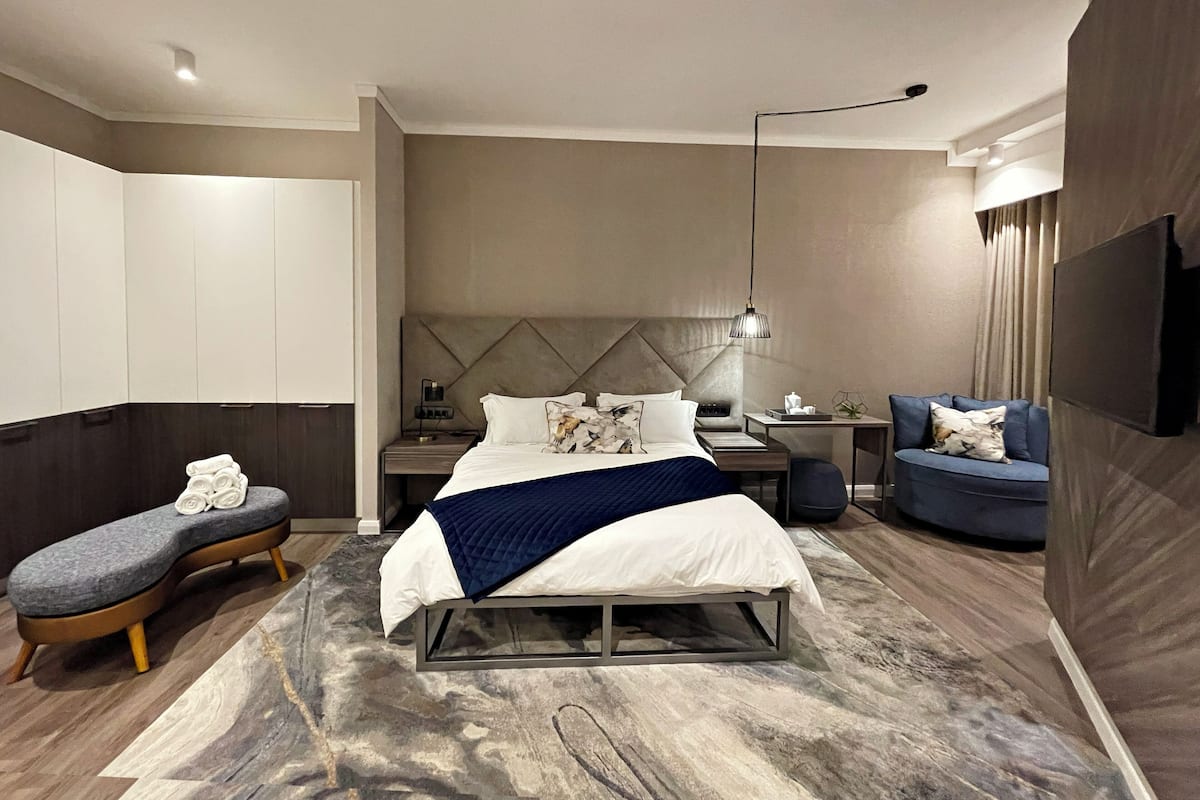 A modern hotel room with a large bed, a desk, a seating area, and a TV.