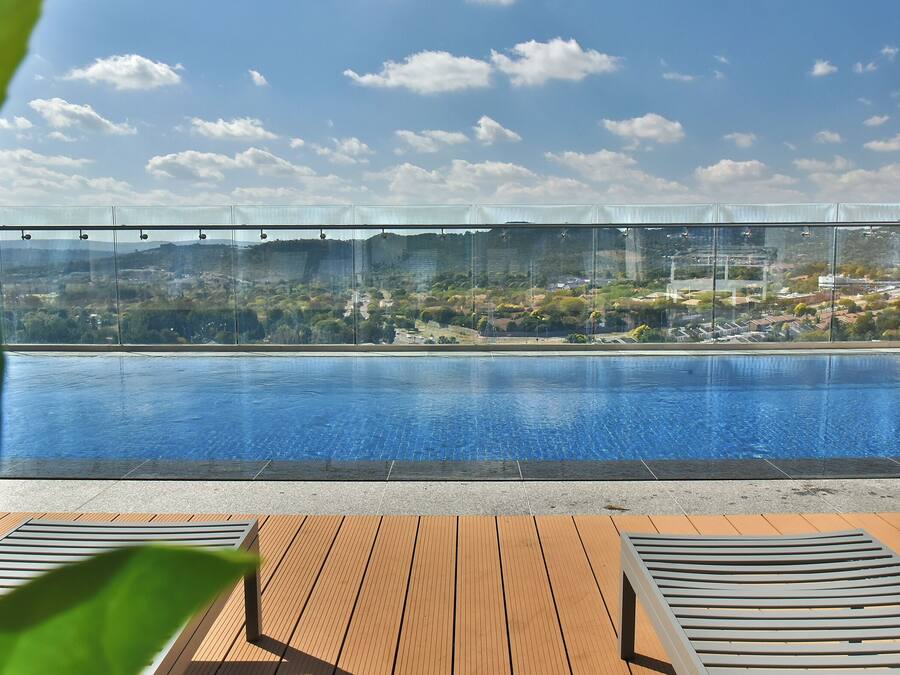 Una piscina infinita con vistas despejadas a una zona residencial y colinas al fondo.