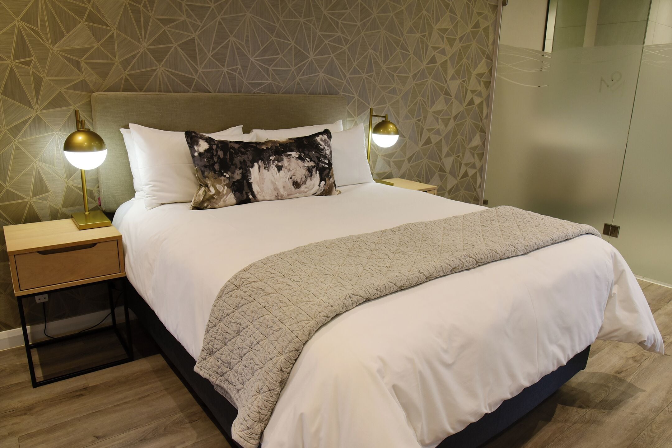 A neatly made bed with a quilted blanket, two bedside lamps, and a nightstand with a drawer.