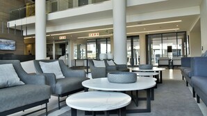 A spacious lobby with grey sofas, round tables, and a large TV screen.