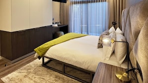 A modern hotel room with a large bed, a desk, a flat-screen TV, and a view of the city through the window.