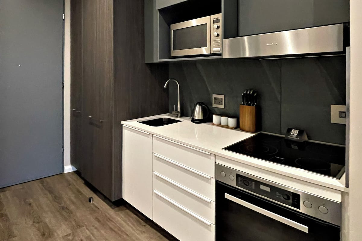 A modern kitchen with a built-in microwave, stove, and oven, white cabinetry, and a wooden floor.