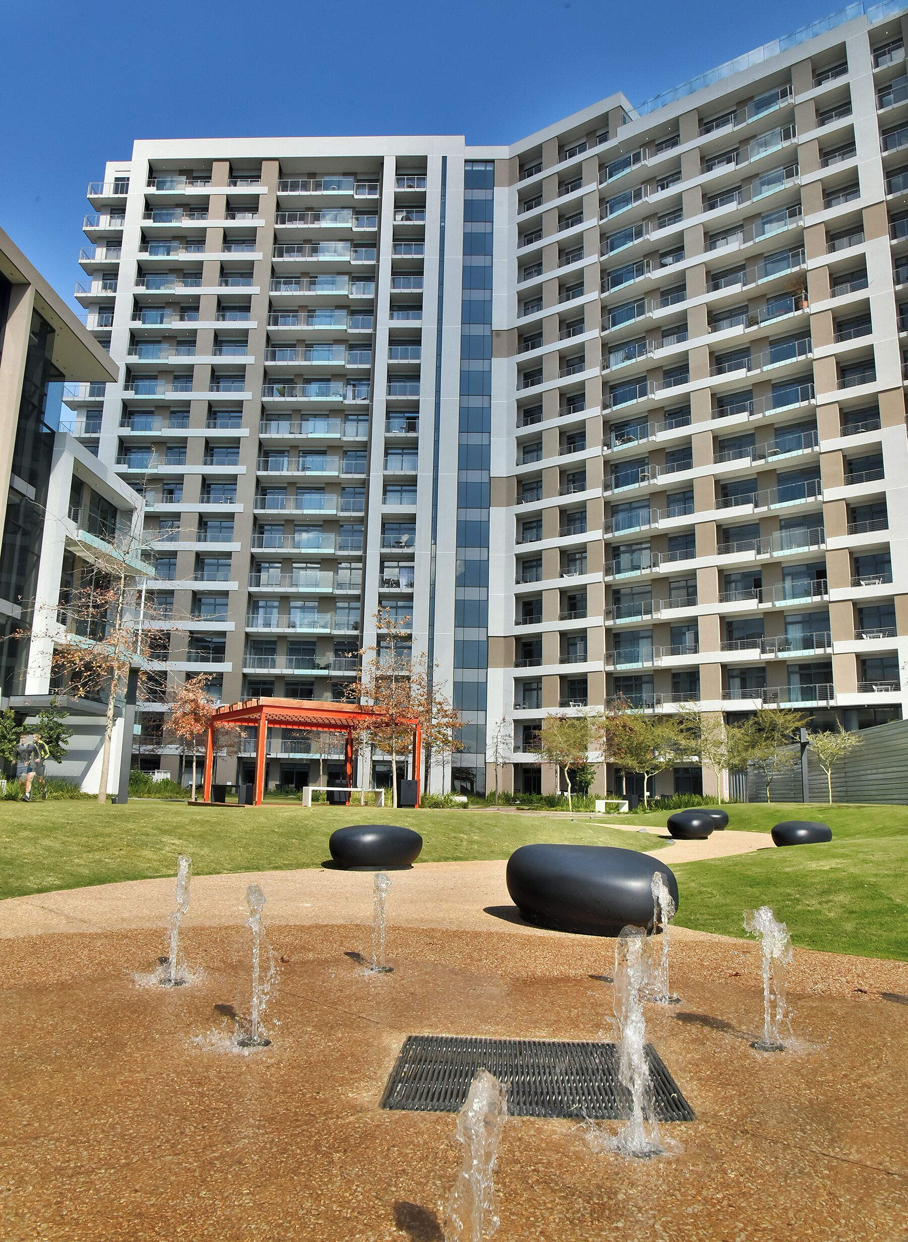 A modern high-rise building with multiple balconies, a central courtyard with water features, and a red pergola.